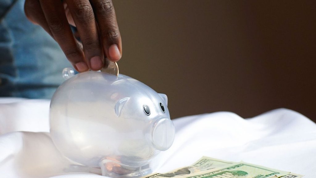 Hand dropping a coin into a glass piggy bank, showing tax on savings interest in the UK