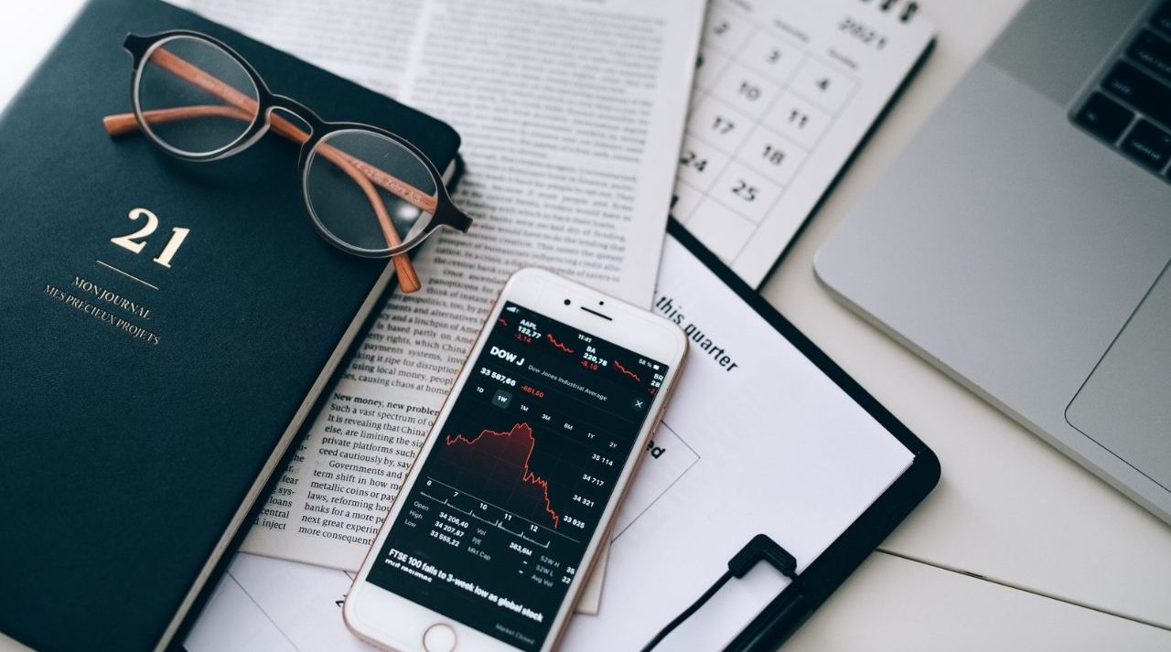 Dividend growth investing UK: smartphone showing a share price chart beside a financial newspaper and glasses